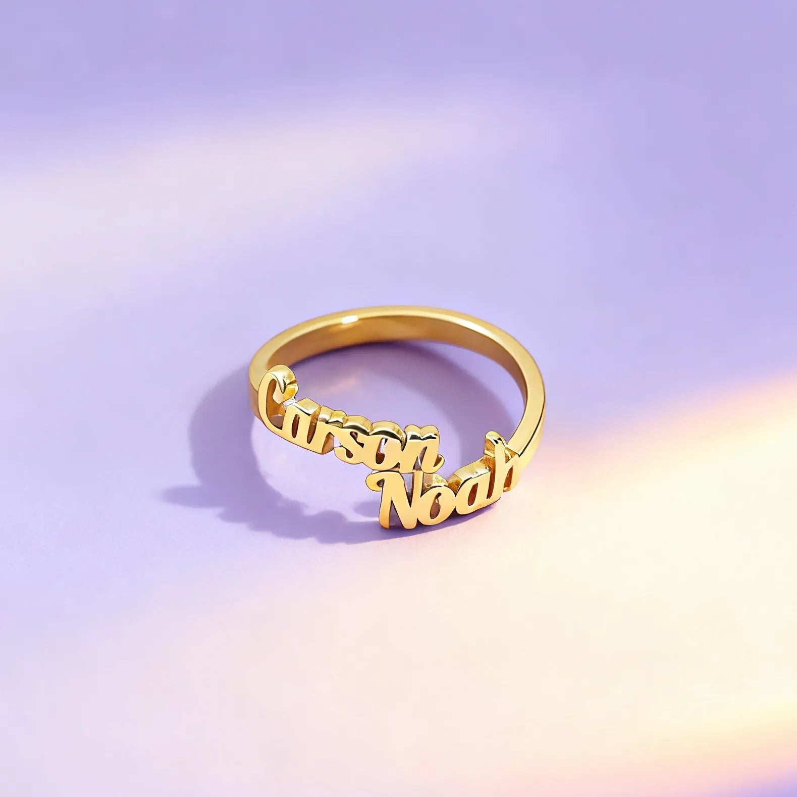 Gold ring with 'Carson Noah' engraving on a gradient purple and pink background
