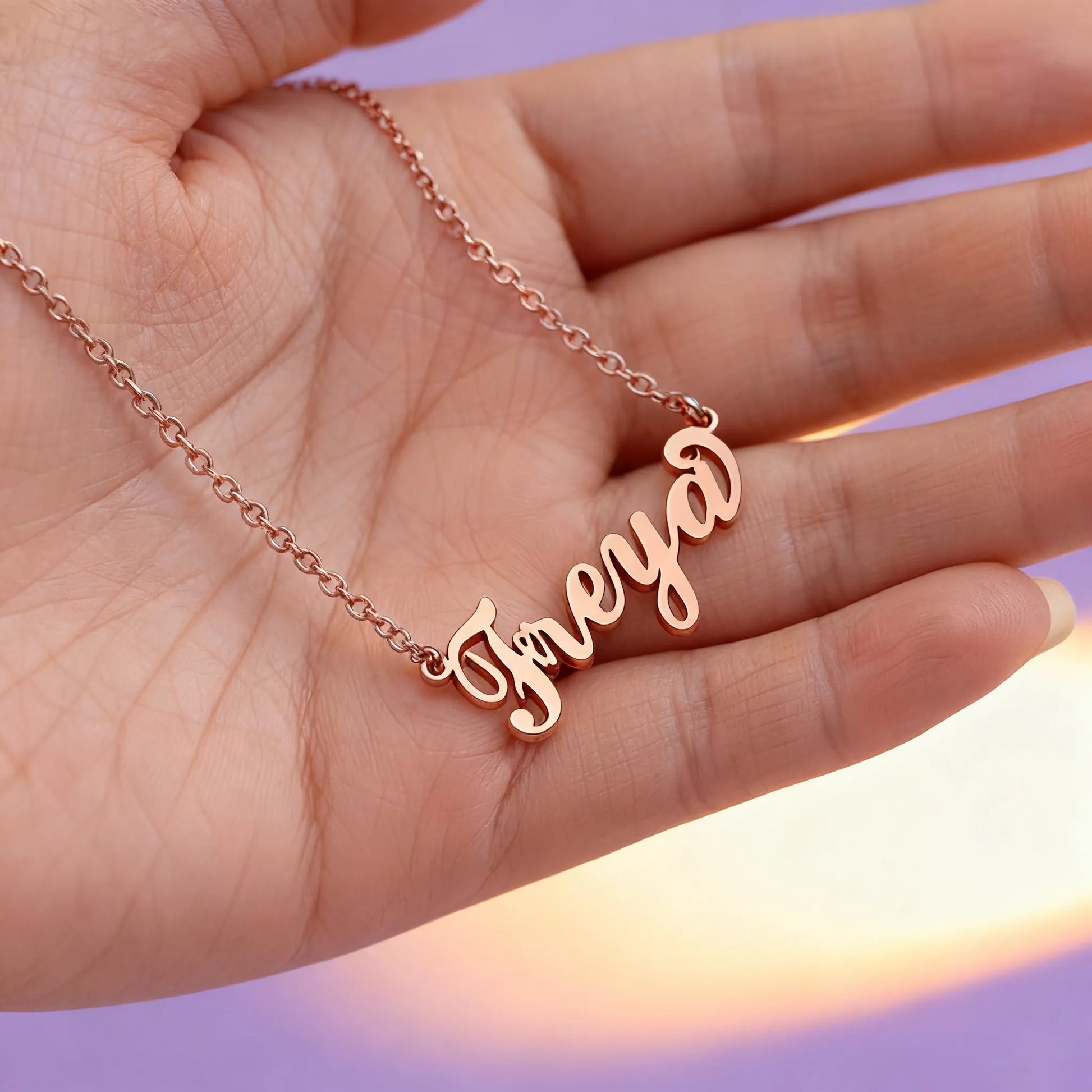 Hand holding rose gold personalized name necklace, cursive lettering close-up